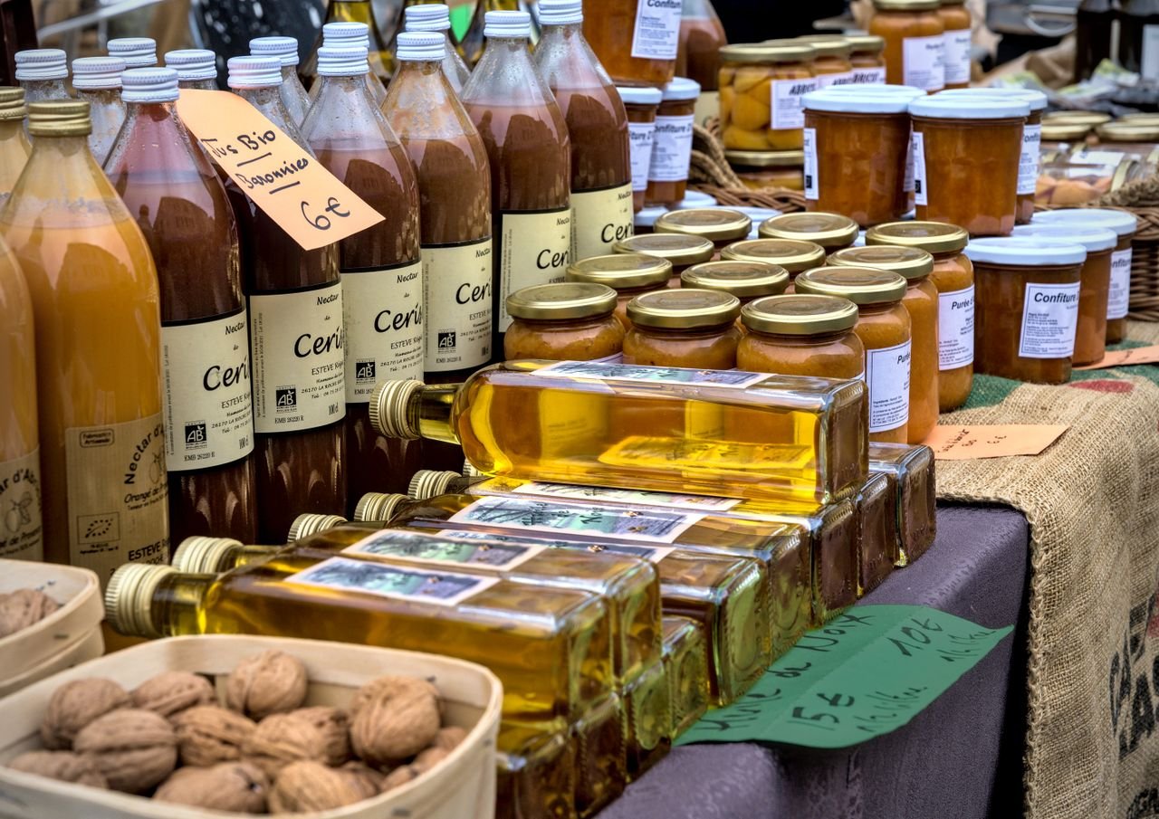 Services Fresh organic juices, oils, and preserves displayed at a vibrant French market stall.