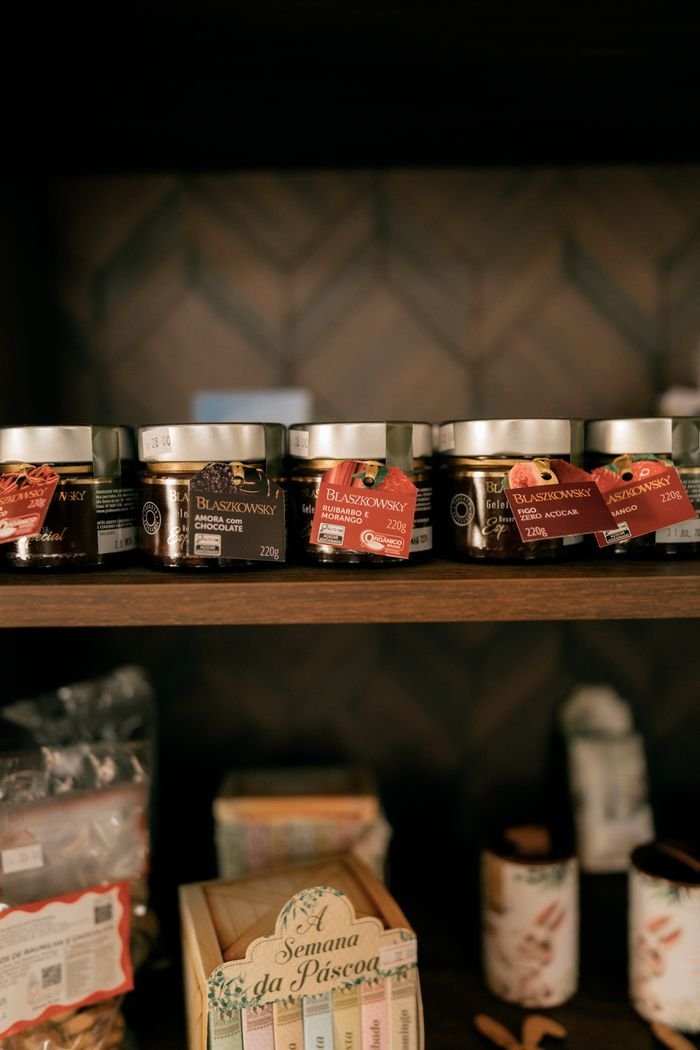 Assorted jars of jam displayed on a wooden shelf in a rustic setting.